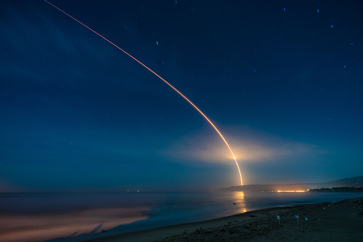 a long exposure night photo shows the trail of a launched rocket across the sky